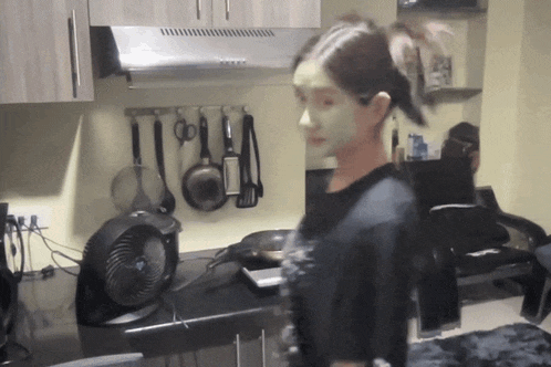 a woman with a green mask on her face stands in front of a kitchen counter