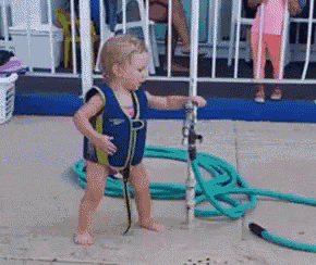 a little girl in a speedo is standing in front of a hose