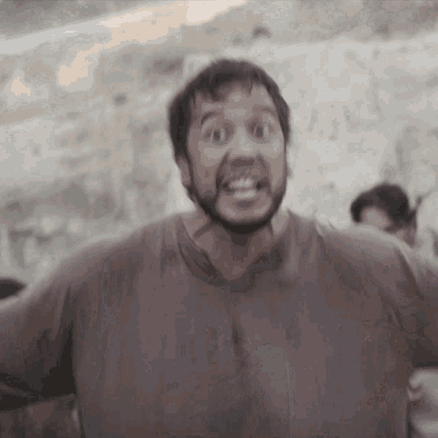a man with a beard wearing a brown shirt is making a funny face