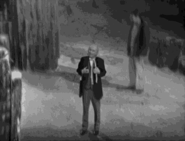 a man in a suit and tie is standing in a dark room with a microphone in his hand .