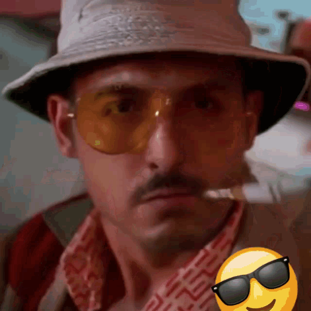 a man wearing a hat and sunglasses smoking a cigarette next to a smiley face