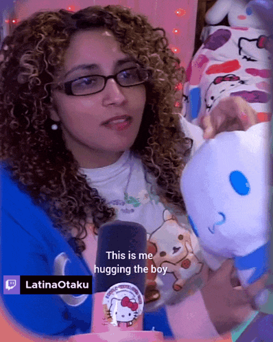 a woman with curly hair and glasses is hugging a stuffed hello kitty