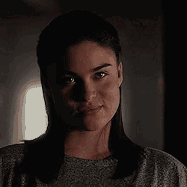 a close up of a woman 's face in a dark room with a window in the background .