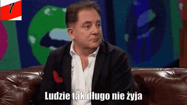 a man in a suit sits on a couch with the words ludzie tak długo nie zyja written below him