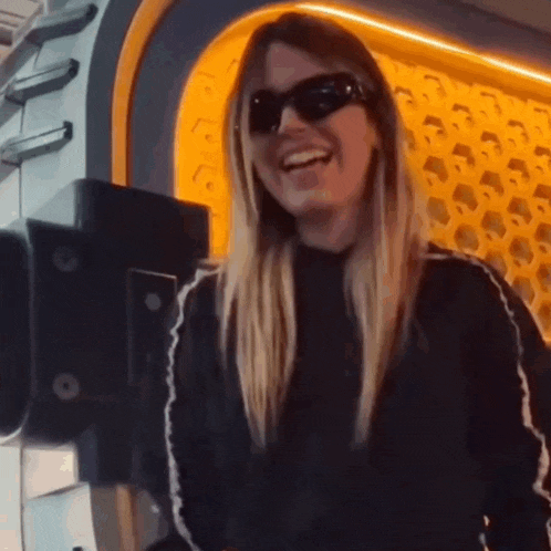 a woman wearing sunglasses and a black sweater is laughing .