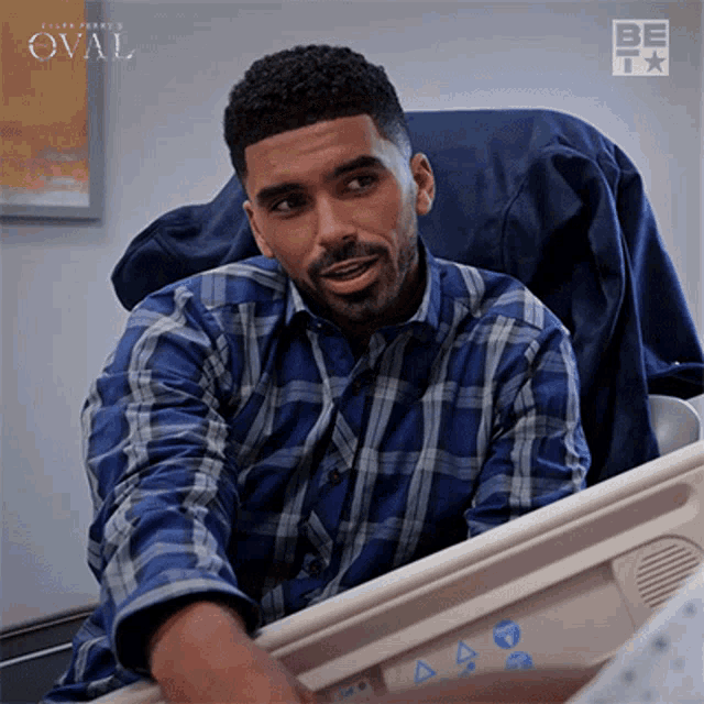 a man in a blue plaid shirt is sitting in a hospital bed talking to someone