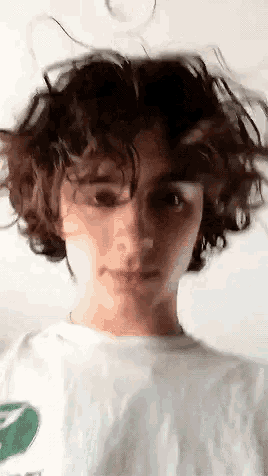 a young boy with curly hair is standing in front of a white wall .