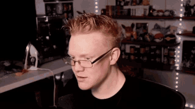 a man with red hair and glasses is sitting in front of a computer screen .