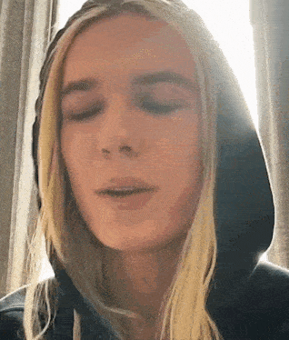 a close up of a woman wearing a hoodie with her eyes closed .