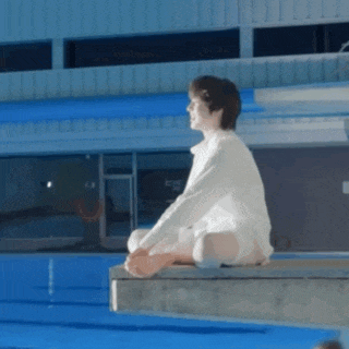 a man in a white shirt sits on a diving board near a swimming pool