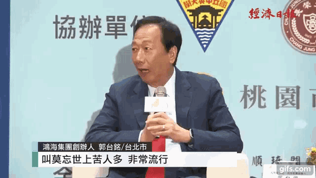 a man in a suit speaking into a microphone in front of a sign that says chung fang