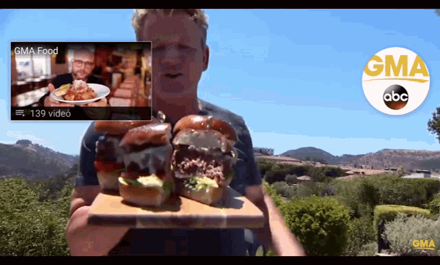 a man is holding two hamburgers in front of a gma food video