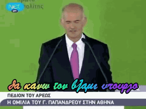 a man in a suit and pink tie is giving a speech in greek