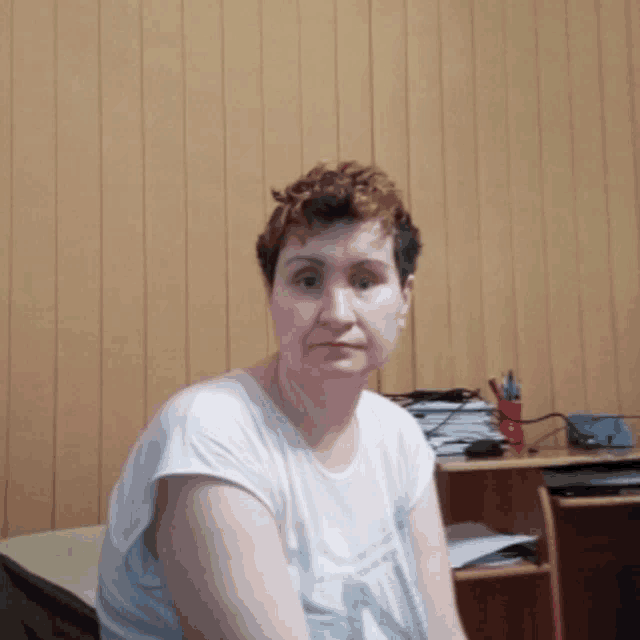 a woman in a white shirt sitting in front of a wood paneled wall