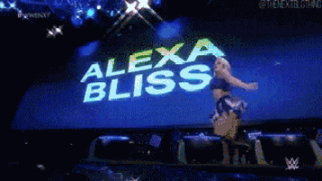 a woman is dancing on a stage in front of a alexa bliss sign
