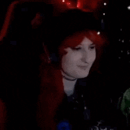 a woman wearing a red wig and headphones is sitting in a chair .