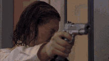 a man with long hair is holding a gun in his hand and pointing it at the camera .