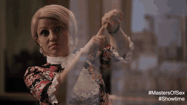 a woman in a floral dress is making a gesture with her hands in front of a screen that says masters of sex