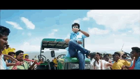 a man is sitting on the back of a green tractor surrounded by people