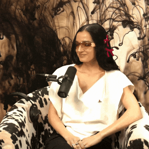 a woman wearing sunglasses sits in a chair with a microphone