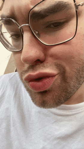 a man wearing glasses and a white shirt is making a face