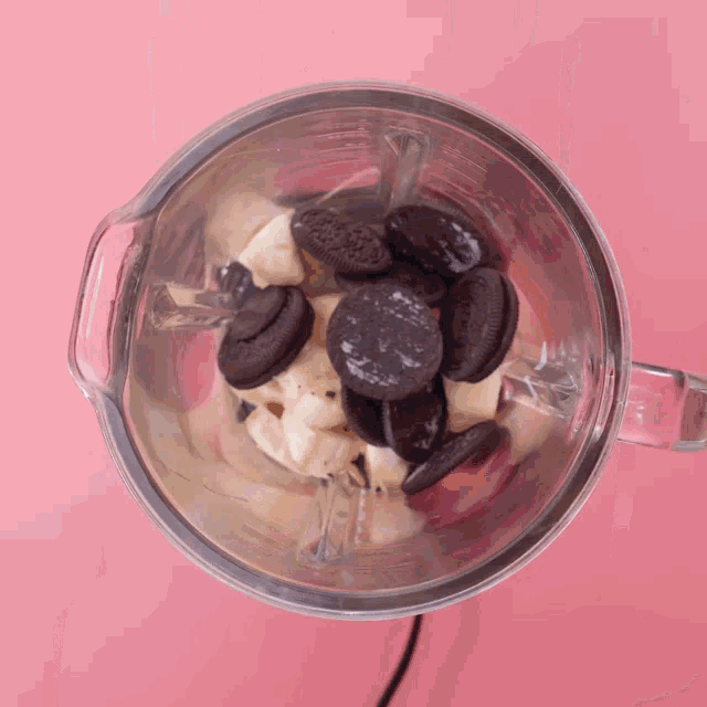 a blender filled with oreos and chocolate butter on a pink background