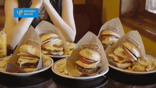 a woman sitting at a table with plates of hamburgers and a sign that says odyssey books on it