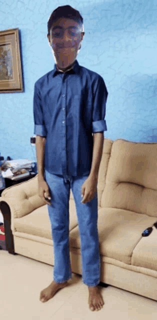 a young man in a blue shirt and jeans stands in front of a couch
