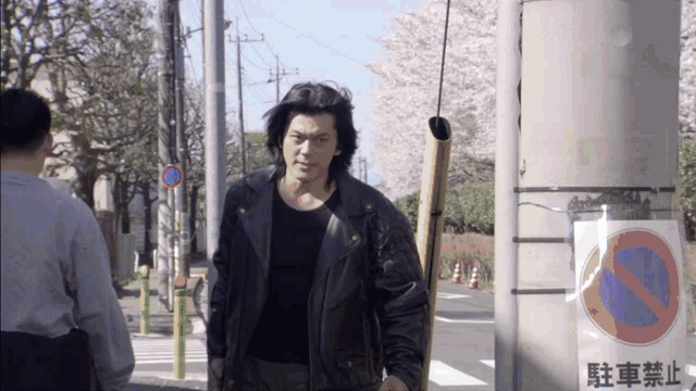 a man in a leather jacket walks down a street next to a sign that says no parking