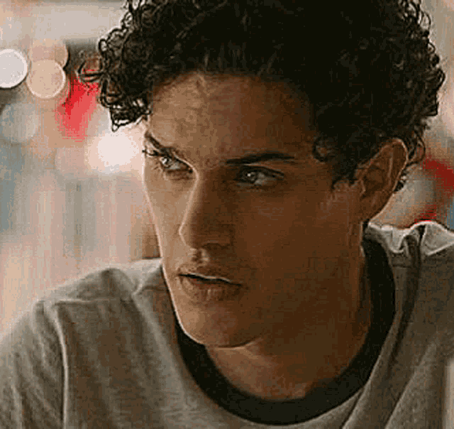 a close up of a young man with curly hair wearing a gray t-shirt .