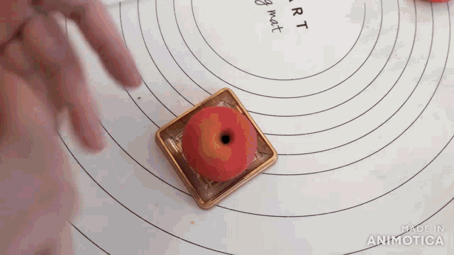 a person 's hand is reaching for a red apple in a box on a mat that says made in animotica