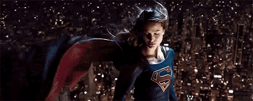 a woman in a superhero costume is flying over a city at night .