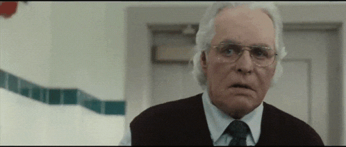 an older man wearing glasses and a vest is standing in a bathroom
