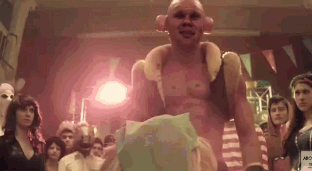 a man without a shirt is standing in front of a crowd of people in a room .