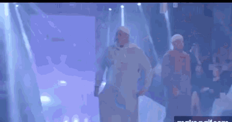 a man in a white shirt is walking down a runway in front of a crowd .