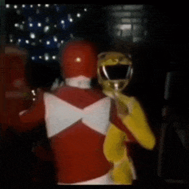 a red and yellow power ranger are dancing together in a dark room .