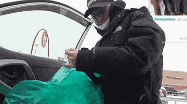 a man wearing a black jacket and a black adidas hat is holding a green bag