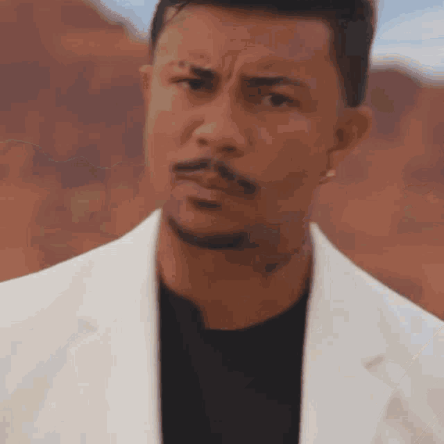 a man with a beard is wearing a white jacket and black shirt