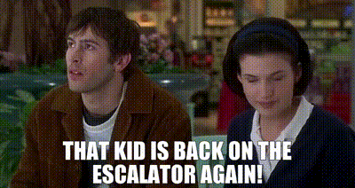 a man and a woman are sitting next to each other in a mall and the man is saying that kid is back on the escalator