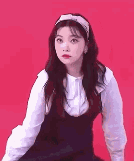 a young woman wearing a headband and a white shirt is sitting on a red background .