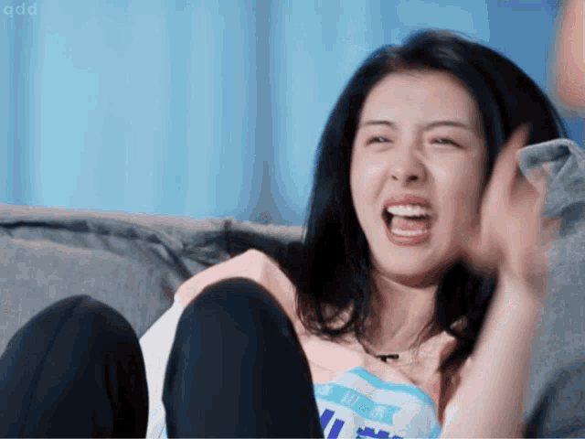 a woman sitting on a couch wearing a shirt that says ' qqd ' on the bottom