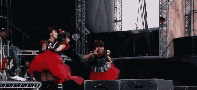 three girls in red dresses are dancing on a stage at a concert .