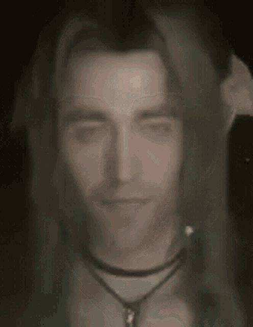 a close up of a man 's face with long hair and a necklace .