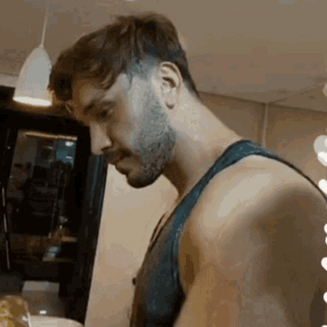 a shirtless man with a beard is standing in a room looking down .