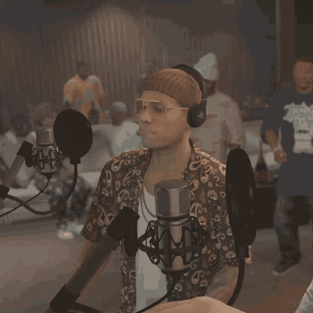a man wearing headphones and sunglasses stands in front of a microphone