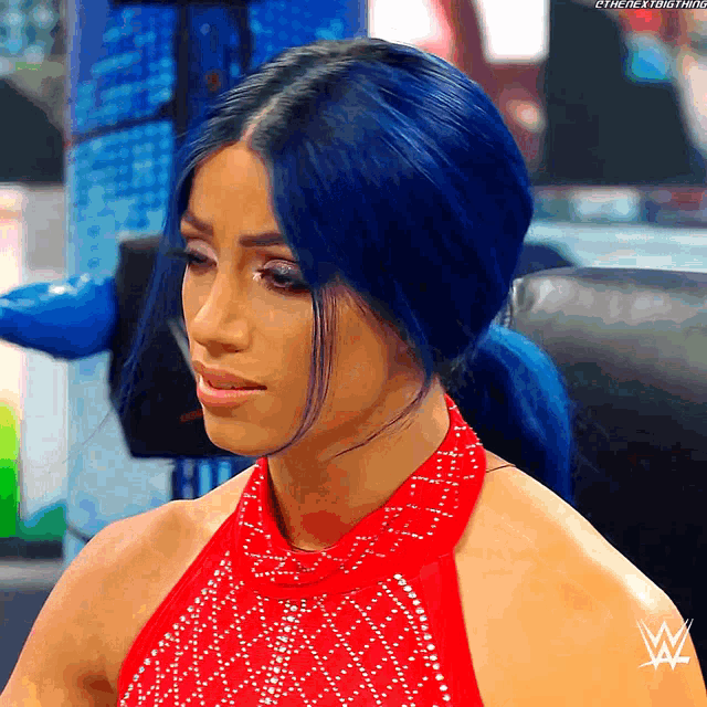 a woman with blue hair is wearing a red dress with a w logo on her arm
