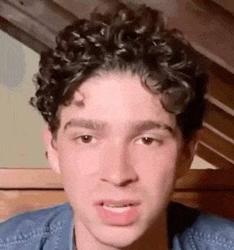 a young man with curly hair is making a funny face while sitting in a chair .