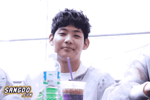 a young man is drinking from a plastic cup with a straw and a bottle of water in the background