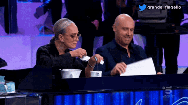 a man and a woman are sitting at a table with a twitter logo in the background