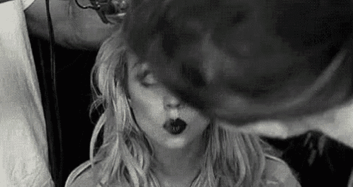 a black and white photo of a woman blowing a kiss while getting her hair done .
